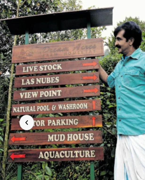 Vinod standing near the Dream Acres farm welcome board in Poovaranthodu